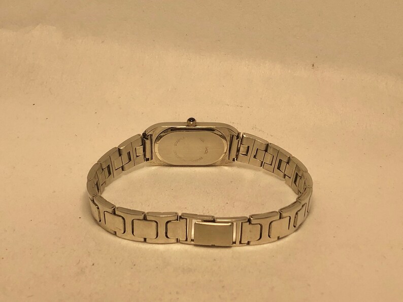 Puede incluir: Un reloj plateado con una esfera rectangular y una correa de metal plateado.