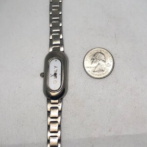 Puede incluir: Un reloj plateado con una esfera blanca y la palabra "DIALY" impresa en &eacute;l. El reloj tiene una pulsera de metal plateado.