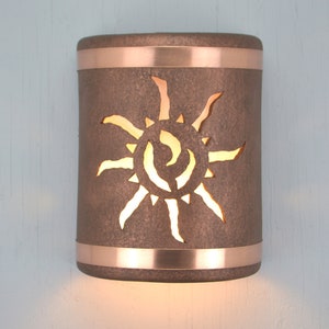 May include: A copper wall sconce with a sun design cut out. The sconce has a brown finish and a copper band around the top and bottom.