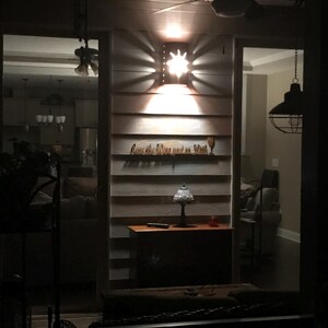 May include: A wooden sign with the text "Love the wine you're with" and a wine glass icon. The sign is lit by a star-shaped light fixture. The sign is mounted on a wall with horizontal wood planks.