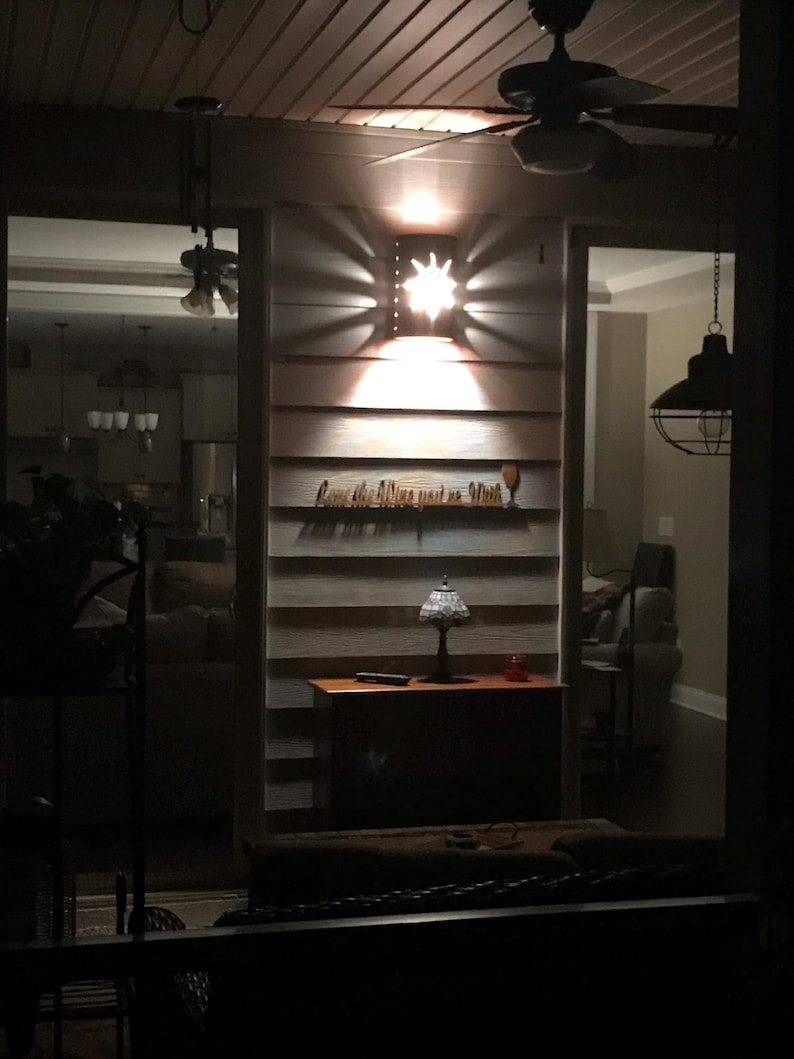 May include: A wooden sign with the text "Love the wine you're with" and a wine glass icon. The sign is lit by a star-shaped light fixture. The sign is mounted on a wall with horizontal wood planks.
