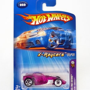 May include: A Hot Wheels X-Raycers die-cast toy car in its original packaging. The car is a transparent magenta color with silver exhaust pipes. The packaging is blue with the Hot Wheels logo and the text "X-Raycers 10/10". The package is 6 inches tall.