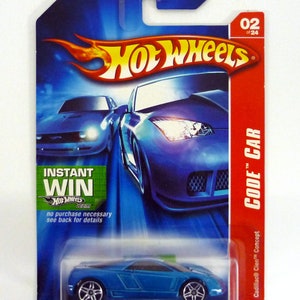 Op de afbeelding: Een blauwe Hot Wheels speelgoedauto in een blisterverpakking. De auto is een Cadillac Cien Concept Code Car. De verpakking heeft de woorden "Instant Win" en "Hot Wheels.com" erop. De auto is nummer 02 van 24.