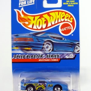 May include: A blue Hot Wheels die-cast toy car in a plastic package. The car is a Mustang Cobra and is part of the Speed Blaster series. The package has the words "Guaranteed for Life" and "Watch Petty Race".