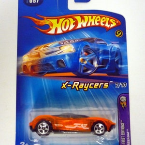 Op de afbeelding: Oranje Hot Wheels X-Raycers speelgoedauto op een blauwe kaart met de tekst "X-Raycers 7/10" en "2005 First Editions™ PHASTASIM™".