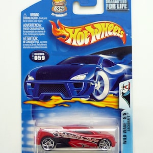 Peut inclure: Une voiture jouet Hot Wheels bleue et rouge dans un emballage en plastique. La voiture est une Backdraft Wild Wave 5/5 rouge et noire. L'emballage porte le logo Hot Wheels et les mots "Garantie à vie".
