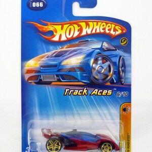 以下が含まれることがあります： 金色のホイールが付いた赤と青のホットウィールトラックエースダイキャスト製おもちゃの車。この車はオープンロードスターで、10台の車のシリーズの一部です。パッケージは青で、ホットウィールのロゴが特徴です。