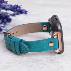May include: Teal leather watch strap with rose gold hardware and a black watch face.
