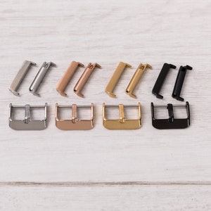 May include: Four pairs of watch strap buckles in different finishes: silver, rose gold, gold, and black. Each buckle is made of metal and has a polished finish.