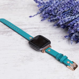 May include: A teal blue leather watch strap with rose gold hardware. The strap is designed for a smartwatch and has a minimalist style.