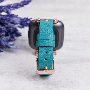 May include: Teal leather watch strap with rose gold hardware and a textured finish.