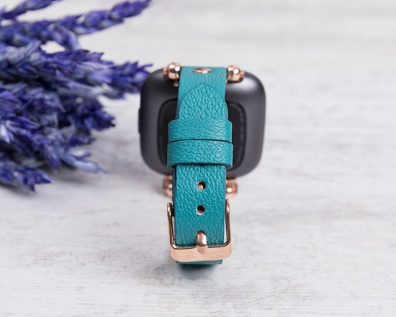May include: Teal leather watch strap with rose gold hardware and a textured finish.