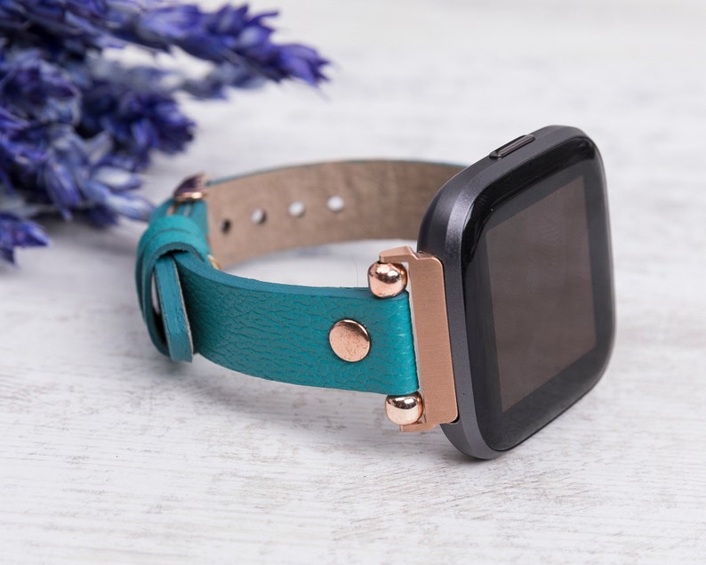 May include: A teal leather watch strap with rose gold accents and a black smartwatch.