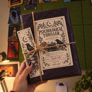 May include: A rectangular book wrapped in dark purple paper, tied with brown twine. A cream-colored label features black ink illustrations of a raven, books, and floral motifs, with the text Psychological Thriller Blind Book and a matching bookmark.