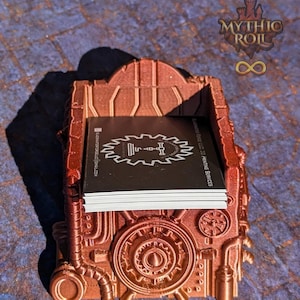 May include: A copper-colored 3D printed dice tower with a steampunk design. The tower has a slot for holding dice and a gear-shaped design on the front. The tower is sitting on a blue and brown patterned surface.