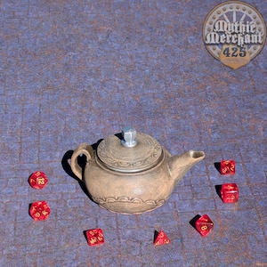 Könnte beinhalten: Eine braune Teekanne aus Keramik mit Deckel und Ausguss, umgeben von sechs roten Würfeln mit goldenen Zahlen auf einer blau-braunen gemusterten Oberfläche. Der Text "Mythic Merchant 425" ist in einem kreisförmigen Zahnrad-Design sichtbar.
