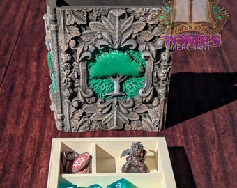 May include: A white wooden box with compartments for dice and miniature figures. The box is decorated with a carved design of a tree. The box is open and there are several green dice inside. The box is sitting on a wooden surface.