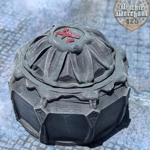 May include: A dark gray, intricately detailed, 3D printed box with a domed lid. The lid features a red symbol on top. The box is sitting on a blue and gray patterned surface.