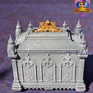 May include: A grey, gothic-style box with ornate detailing. The box features arched windows, decorative spires, and a gold-coloured embellishment on the lid. The Fates End logo is visible in the upper right corner.