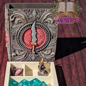 May include: A decorative book-shaped box with a red and gold design. The box is open and contains a miniature figure, dice, and other game pieces. The box is labelled "Fates End 2024-2025 FOMES MERCHANT".