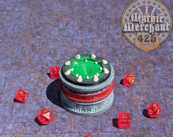 May include: A green and gray tabletop game piece with a red and white base.  The piece is surrounded by six red dice with white numbers.  The dice are scattered around the piece on a gray and blue stone-like surface.  The text "Mythic Merchant 425" is visible in the upper right corner of the image.