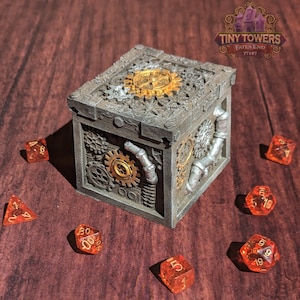 May include: A gray metal box with intricate gears and pipes on the sides. The box is surrounded by six orange dice with gold numbers. The box has the text "TINY TOWERS FATES END TT187" on the top.