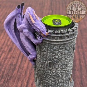 May include: A purple dragon figurine climbing a gray stone tower with a green can lid on top. The tower has a brown base with gold accents.