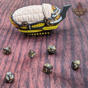 May include: A set of six black and gold dice with white numbers. The dice are on a brown wooden surface. There is a small, yellow and black model of a ship in the background.