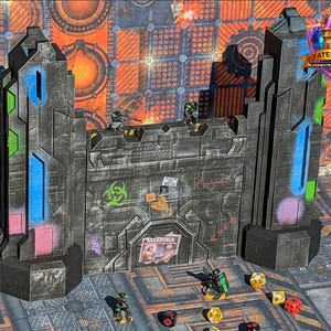 May include: A gray, textured fortress model with blue, green, and pink accents. The model has a weathered appearance and features the text "GUARDIANS" and a biohazard symbol. Several miniature figures and dice are scattered around the base of the fortress.