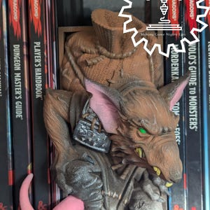 May include: A brown and grey rat figurine with a pink tail, holding a small sack. The figurine is a bookend and is sitting on a shelf with several Dungeons & Dragons books.