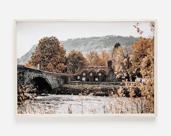 May include: A stone bridge over a river with a small cottage covered in vines in the background. The trees are in autumn colors, with shades of orange, brown, and yellow.