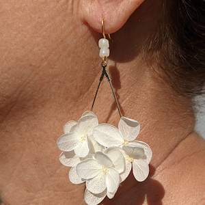 May include: White dried flower earrings with a gold triangle design and white beads hanging from the top.