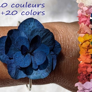 May include: A blue flower bracelet made of dried hydrangeas. The bracelet is on a person's wrist. The image also shows a variety of colors of dried hydrangeas in a rainbow pattern. +20 couleurs +20 colors
