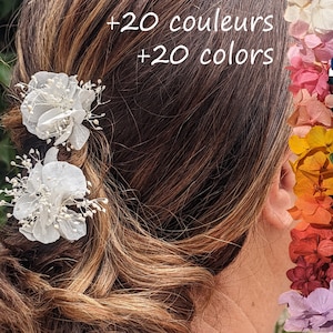 Pode incluir: Dois prendedores de cabelo em forma de flores brancas com pequenas contas brancas. Os prendedores estão no cabelo castanho de uma mulher. A imagem também mostra uma variedade de cores de flores secas.