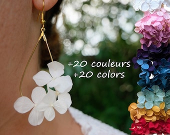May include: White dried flower earrings on a gold teardrop-shaped wire frame. The earrings are shown on a person's ear. The image also shows a rainbow of dried flower colors, with the text '+20 couleurs +20 colors'.