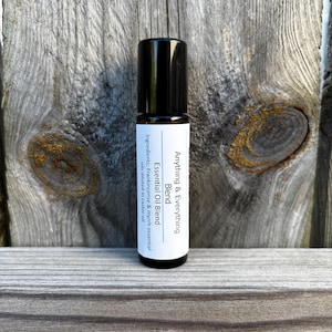 May include: A black roll-on essential oil bottle with a white label against a weathered wood background. The label reads "Anything & Everything Blend Essential Oil Blend" with ingredient details. The bottle is approximately 4 inches tall.
