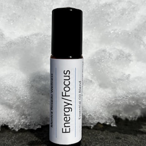 May include: A white roller bottle with a black cap and a white label that reads "Energy/Focus Essential Oil Blend Monica Rosado Wellness".