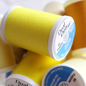 May include: Close-up of spools of yellow, light yellow, and orange thread. The spools are labeled "Dual Duty XP" and "All Purpose".