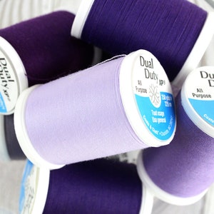 May include: Six spools of thread in shades of purple and lavender. The spools are labeled "Dual Duty XP" and "All Purpose".