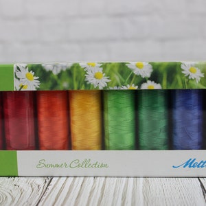 May include: A box of Mettler thread spools in a rainbow of colors. The box has a green border and a floral design with the words "Summer Collection". The thread colors include red, orange, yellow, green, blue, and purple.