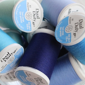 May include: A close-up of a collection of blue, teal, and light blue spools of thread. The spools are labeled "Dual Duty XP" and "All Purpose". Each spool contains 250 yards of thread.
