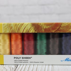 May include: A box of Mettler Poly Sheen thread spools in various colors, including white, yellow, orange, red, green, and blue. The box has a yellow frame and a decorative top. The text "POLY SHEEN" and "Mettler" are visible.