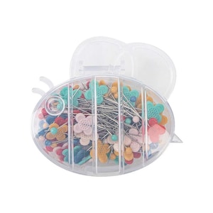 Op de afbeelding: Een doorzichtige plastic container in de vorm van een bij met een compartiment voor het bewaren van naalden. De container is gevuld met kleurrijke bloemvormige naalden.