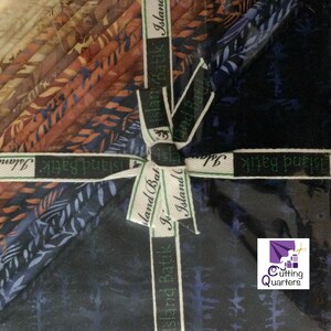 Könnte beinhalten: Ein Bündel Stoffquadrate in Blau-, Braun- und Orangetönen, gebunden mit einem Band mit der Aufschrift "Island Batik". Der Stoff hat ein Blattmuster. Das Logo von Cutting Quarters befindet sich in der unteren rechten Ecke.