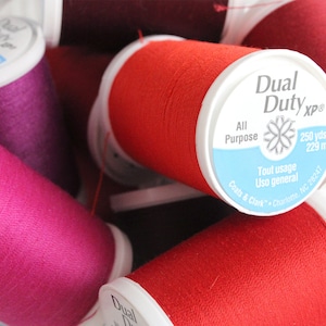 May include: Close-up of spools of red, pink, and purple thread. The label on one spool reads "Dual Duty xp" with the text "All Purpose" and "250 yds/v 229 m".