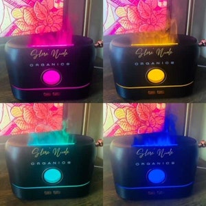 May include: A black rectangular essential oil diffuser with a rounded top and a central circular light. The device features the text 'Shere' Nicole ORGANICS' printed in white and emits a colored mist effect in pink, yellow, teal, or blue.