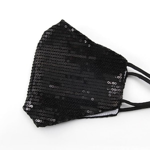 May include: A black face mask with a sparkly sequin design. The mask has two black elastic ear loops.