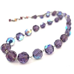May include: A purple iridescent crystal bead necklace with a silver chain. The beads are faceted and have a shimmery finish.