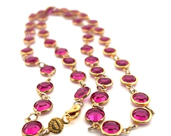 May include: A gold chain necklace with pink round stones. The necklace has a clasp closure.