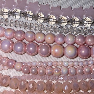 May include: Close-up of various strands of pink beads. The beads include faceted crystals, star-shaped beads, and round pearls in varying sizes. The color palette is soft and feminine, with a range of pink hues.